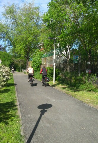 Zwei Radfahrerinnen auf neu asphaltiertem Radweg. Dahinter ein Bolzplatz.