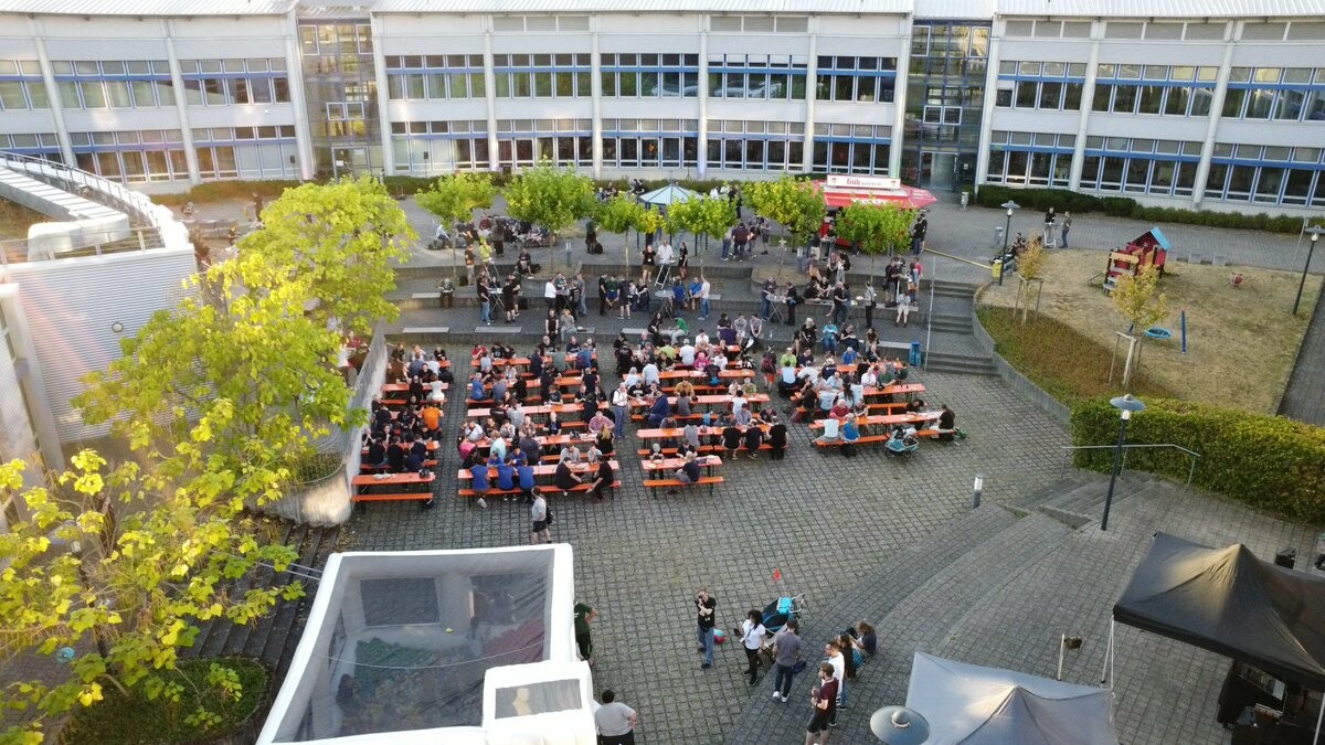 FrOSCon Social Event, Menschen auf Bierbänken im Innenhof der Hochschule Bonn-Rhein-Sieg