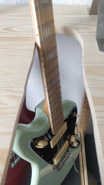 Blick auf ein Holzbrett mit Schlitz. Im Schlitz lehnt eine E-Gitarre. Die Kante dieses Schlitze ist sehr sehr krumm zugeschnitten. 