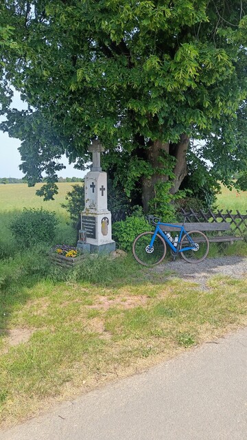 Ein Wegekreuz unter einem Baum, daneben eine Sitzbank, daran gelehnt mein blaues Rennrad