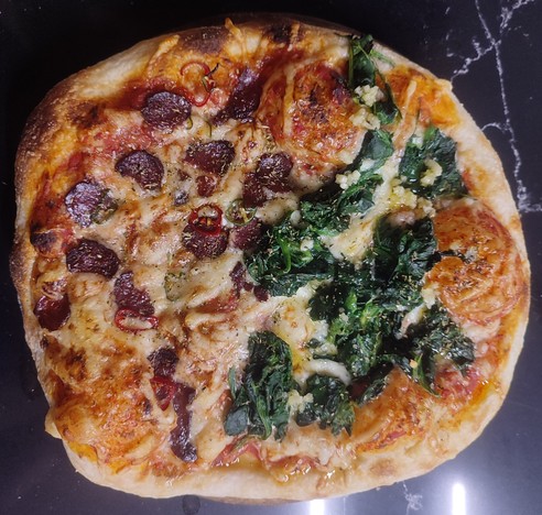 Eine selbstgemachte Pizza mit Salami und Spinat belegt auf eine Arbeitsplatte aus Stein.