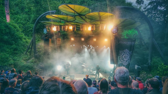 Blick aus erhöhter Position über Hinterköpfe hinweg auf eine Bühne. Dort spielt die norwegische Band Motorpsycho. Die Bühne selbst steht inmitten von Bäumen.