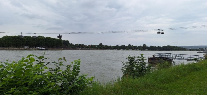 Der Rhein, man sieht einen Teil des Ufers und die Seilbahn in Richtung Festung Ehrenbreitstein über den Fluss.