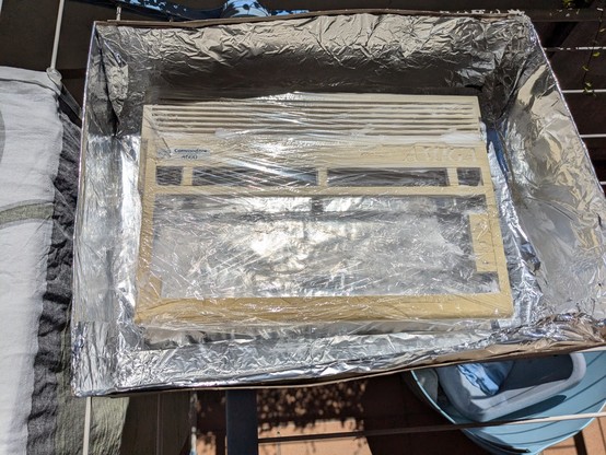 Amiga 600 case in a box with aluminum foil. The case itself is wrapped in transparent foil and wet with hair dye. The case is yellowed over time.