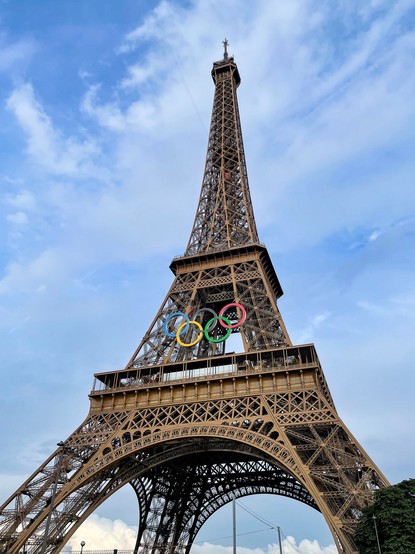 Eiffelturm mit olympischen Ringen gegen einen teilweise bewölkten Himmel.