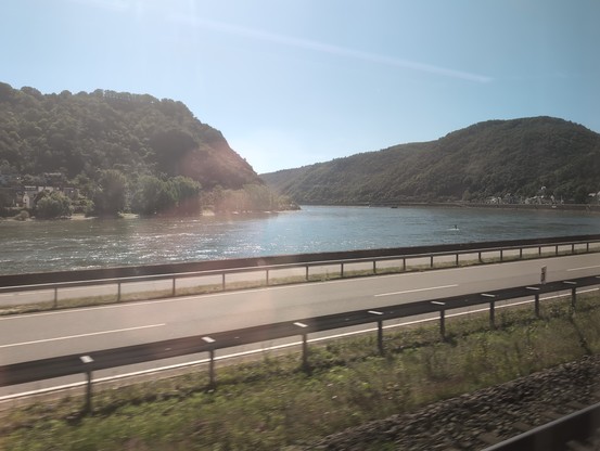 Blick aus dem Zug auf den Rhein mit einer Straße in Bildvordergrund