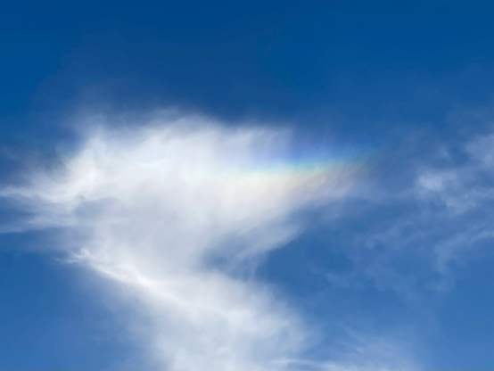 Schönwetterwolke mit einem Regenbogenstreifen am blauen Himmel 