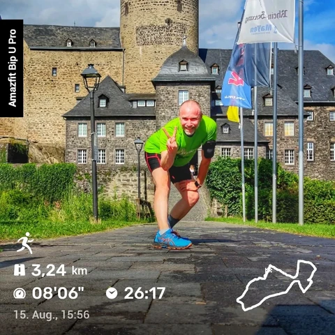 Das Bild zeigt einen Mann, der sich in sportlicher Kleidung, speziell in einem grünen T-Shirt, in einer Pose für ein Foto positioniert. Er zeigt mit seiner Hand das Peace-Zeichen. Im Hintergrund ist eine Burg zu sehen, was darauf hindeutet, dass das Foto vor einer historischen Anlage aufgenommen wurde. 

Die Szene spielt sich offenbar an einem sonnigen Tag ab, da der Himmel blau und klar ist. Der Mann scheint gerade einen Lauf beendet zu haben, wie die Anzeige im Bild vermuten lässt: Er ist 3,24 km gelaufen, mit einer Pace von 8 Minuten und 6 Sekunden pro Kilometer, und die gesamte Laufzeit betrug 26 Minuten und 17 Sekunden. Die Aufnahmezeit ist ebenfalls vermerkt: 15. August, 15:56 Uhr. 

Das Bild wurde mit einer Amazfit Bip U Pro aufgenommen, wie an der Seitenbeschriftung zu erkennen ist.