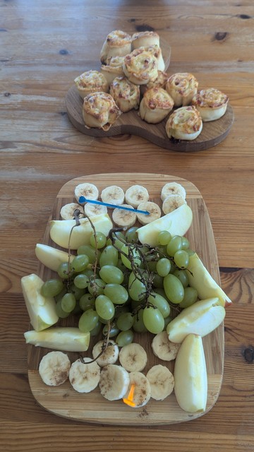 Auf einem Tisch stehen eine gemischte Obstplatte und ein Brett mit gebackenen Schnecken.