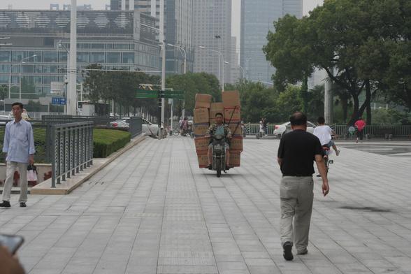 Eine Person in Wuhan (China) mit einem Motorroller, auf dem gut 15 Kartons transportiert werden.
