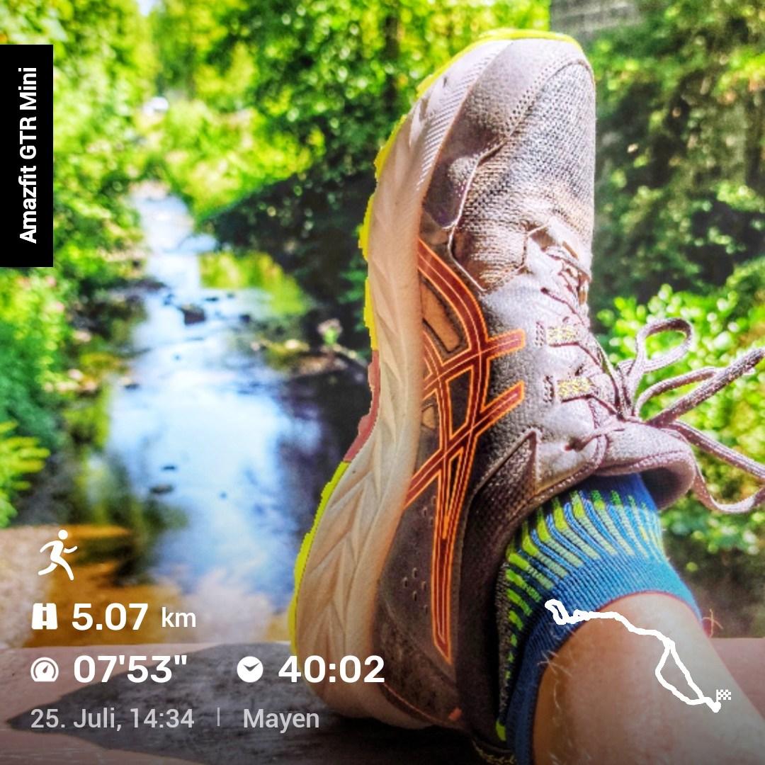 Nahaufnahme eines Laufschuhs mit orange‑gelben Akzenten und blaugrüner Socke, aufgenommen vor einem kleinen Bach mit dichtem grünen Bewuchs. Unten im Bild sind Laufdaten eingeblendet: 5,07 km, Pace 07:53 min/km, Dauer 40:02, aufgenommen am 25. Juli um 14:34 in Mayen. Rechts unten ist eine kleine Karte der gelaufenen Strecke zu sehen.